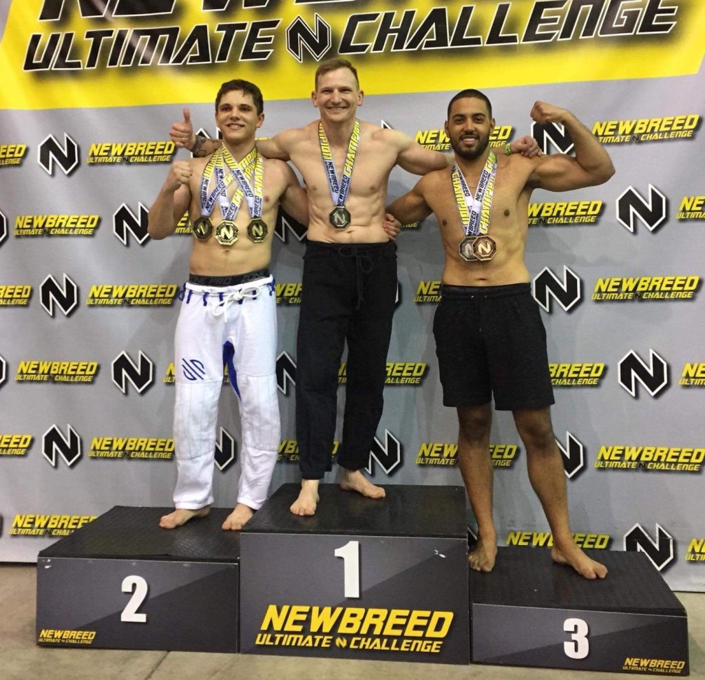 Three male fighters have posed barefoot at the top of the Newbreed Ultimate Challenge podium. From left to right, they are...